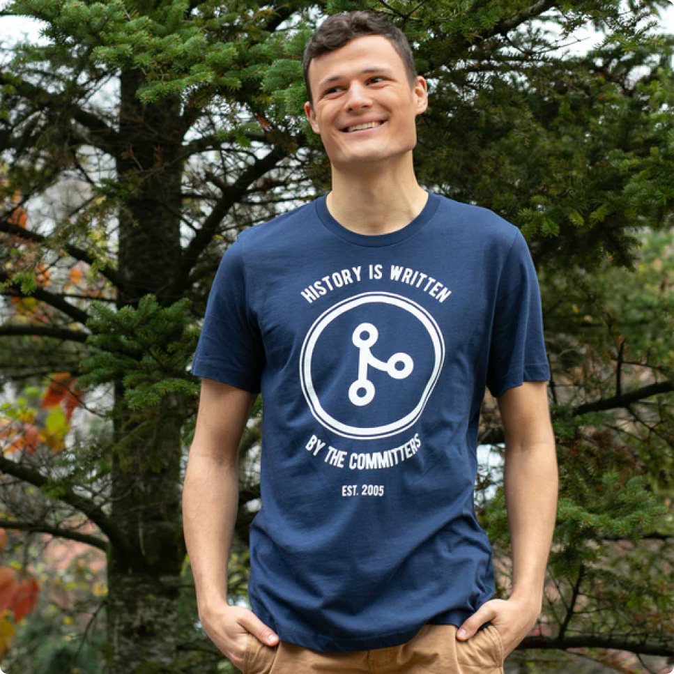 Hombre alto usando polo con el logo de git, que dice 'History is written by the commiters'